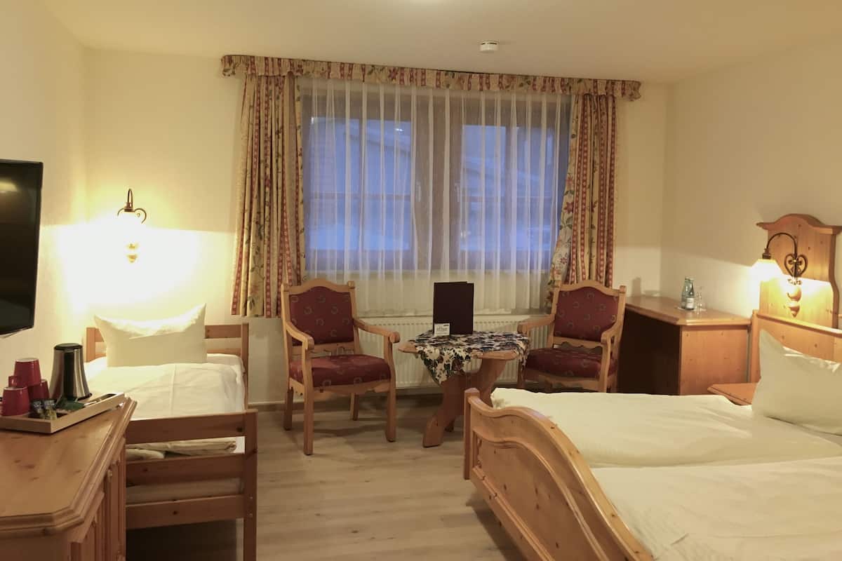 Une chambre d’hôtel avec un lit, deux chaises, une table, un téléviseur et une fenêtre avec des rideaux.