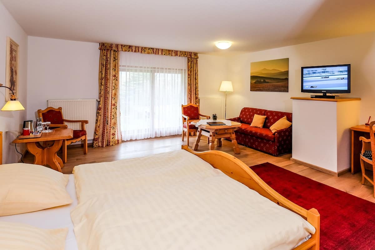 Une chambre d’hôtel équipée d’un lit, d’un bureau, d’une chaise, d’un canapé, d’une télévision et d’une fenêtre avec des rideaux.