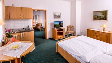 A hotel room with a bed, a desk with a lamp, a chair, a TV, and a painting on the wall.