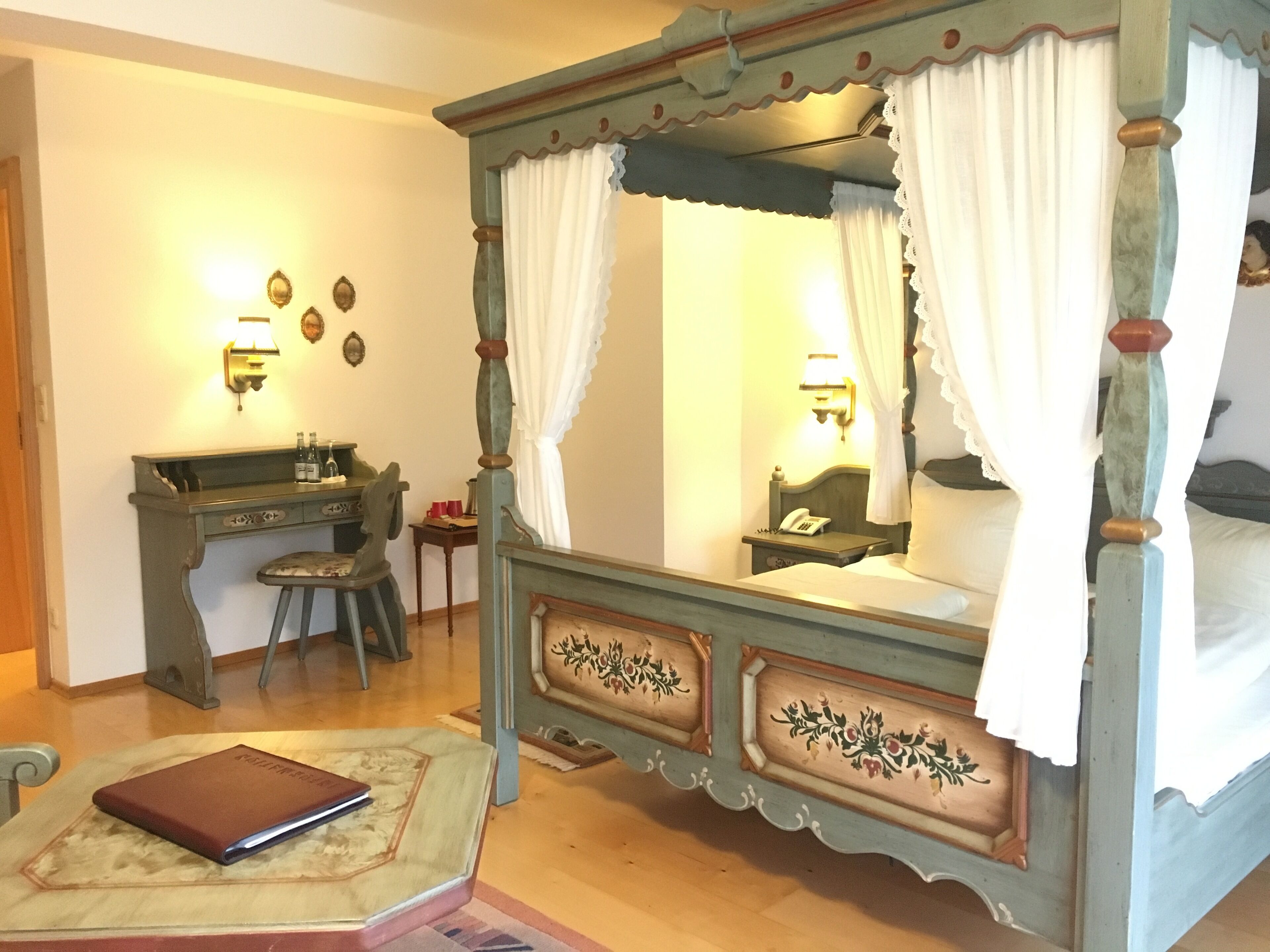 A bedroom with a four-poster bed, a desk, and a chair.