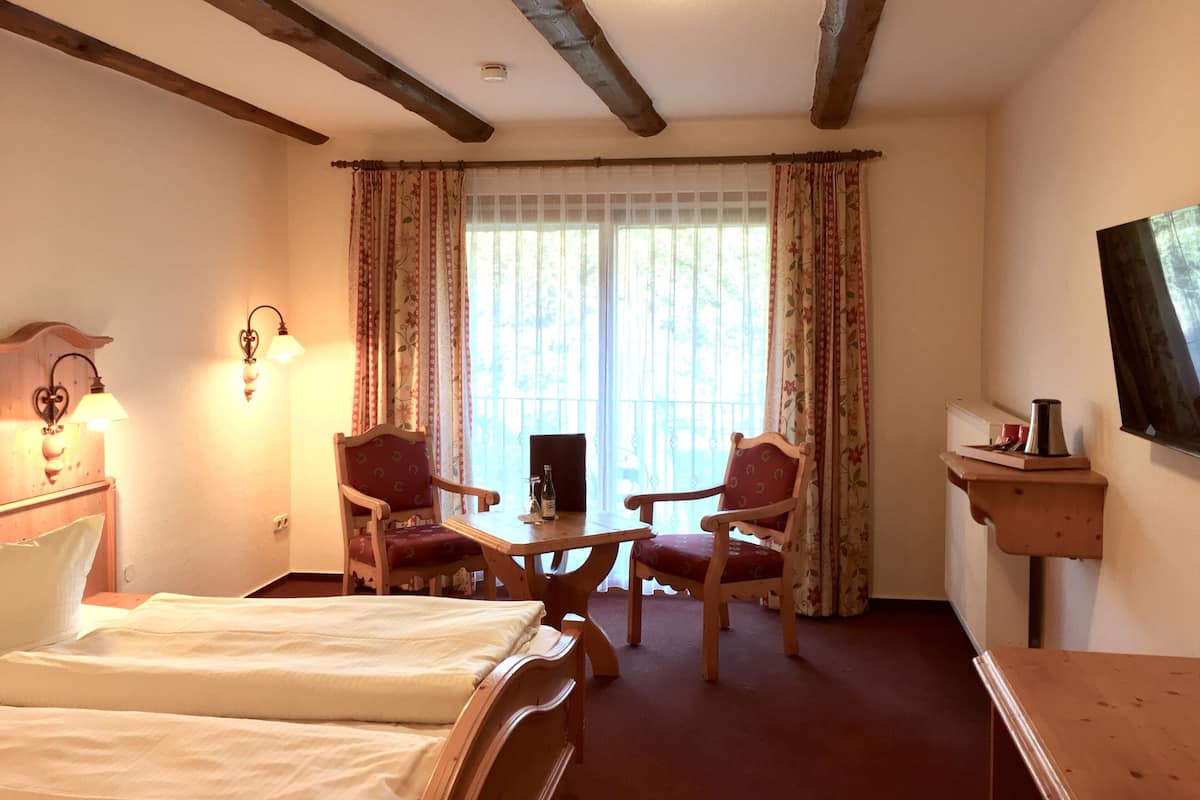 Une chambre d’hôtel avec un lit, deux chaises, une table, un bureau, une télévision et une fenêtre avec des rideaux.