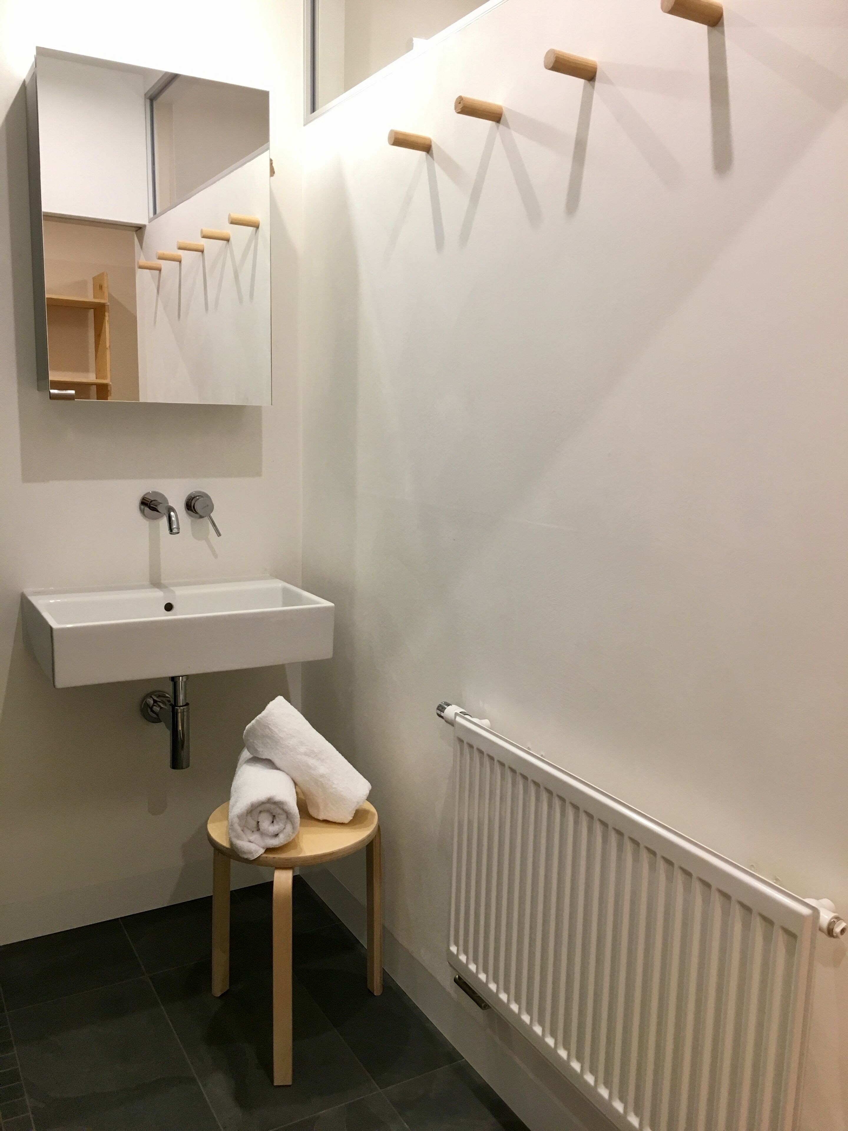 A bathroom with a white sink, a mirror, a towel on a stool, and a radiator.
