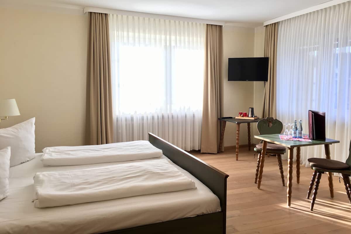 Une chambre d’hôtel équipée d’un lit, d’un bureau, d’une chaise, d’une télévision et d’une fenêtre avec des rideaux.