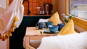 A cozy dining area with a wicker chair, a table set with blue bowls and a yellow cushion, and a hanging light fixture. - Harzer Hof (Herzberg am Harz)