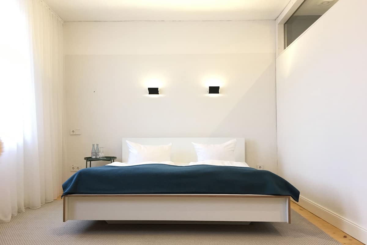 Une chambre moderne avec un lit, deux lampes fixées au mur, une table de chevet et une fenêtre avec des rideaux.