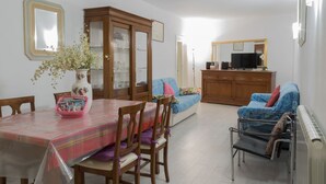 A dining area with a table set for four, a cabinet with glass doors, a sofa, and a television in the background. - Grimaldi Apartments - Jolie (Venice)