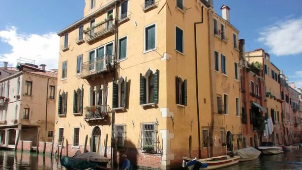 A canal with boats and a yellow building with balconies and shutters. - Grimaldi Apartments - Jolie (Venice)