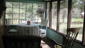 Une pièce avec une grande fenêtre, une table recouverte d’une nappe à motifs floraux et plusieurs chaises.