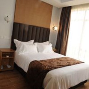 Une chambre d’hôtel avec un grand lit, une tête de lit en bois, une table de chevet et une fenêtre avec des rideaux.