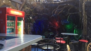 An outdoor seating area with a stone wall backdrop, a red vending machine, and various chairs and tables. - Amelia Hotel Karen (Nairobi)