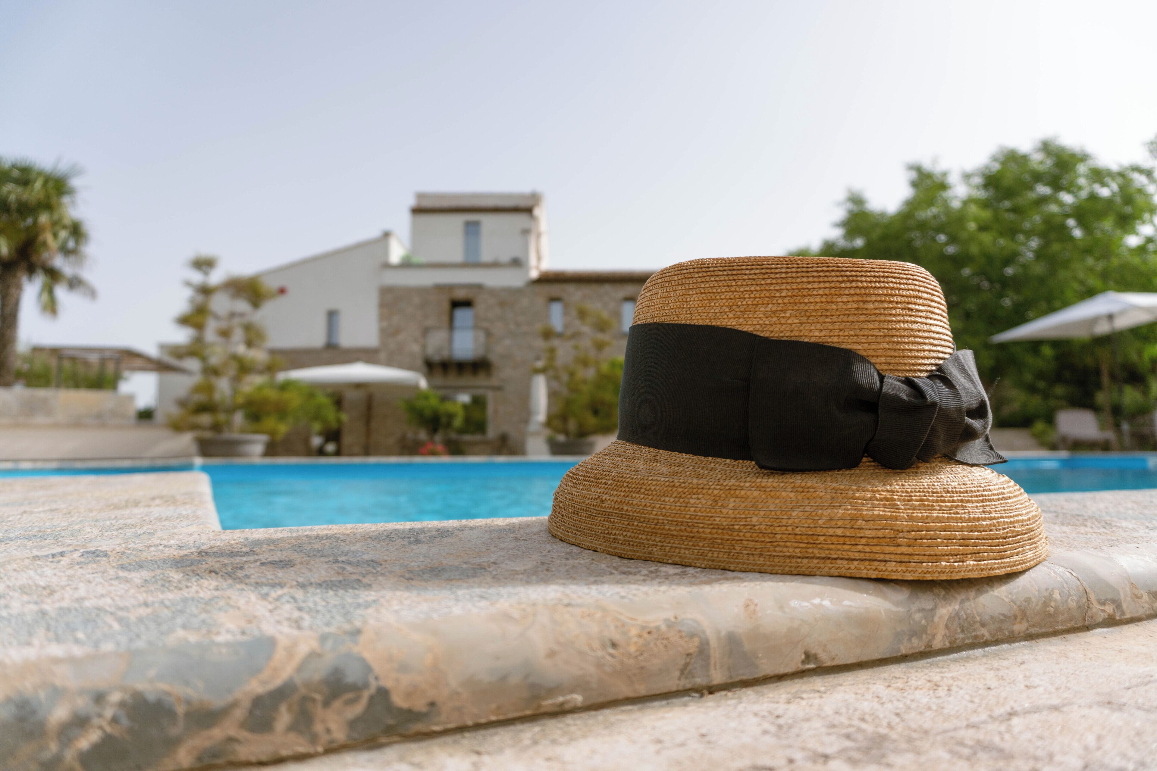 A straw hat on a stone ledge near a pool with a building in the background.