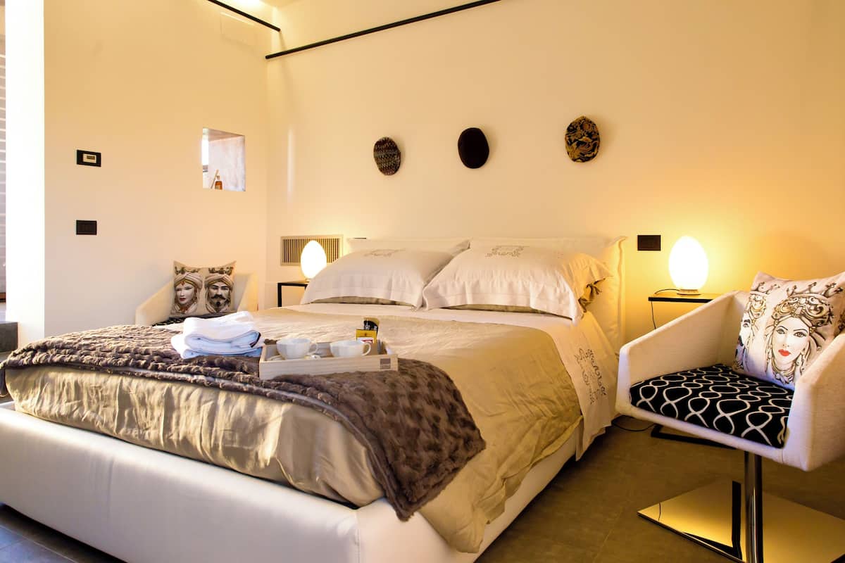 A neatly made bed with a brown blanket, a chair with a patterned cushion, and a bedside table with a lamp.