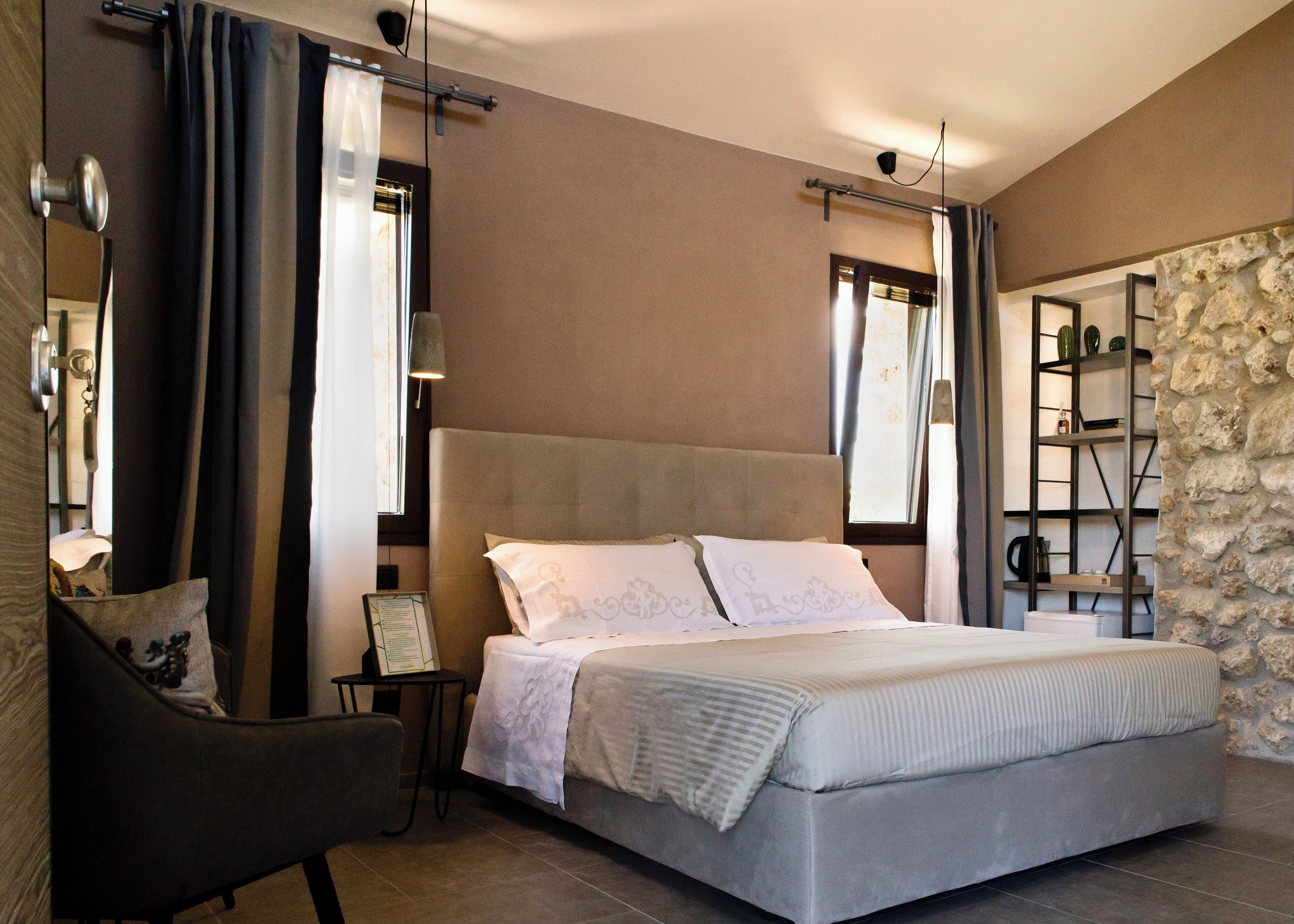 Une chambre avec un grand lit, une chaise, une petite table et un mur en pierre.