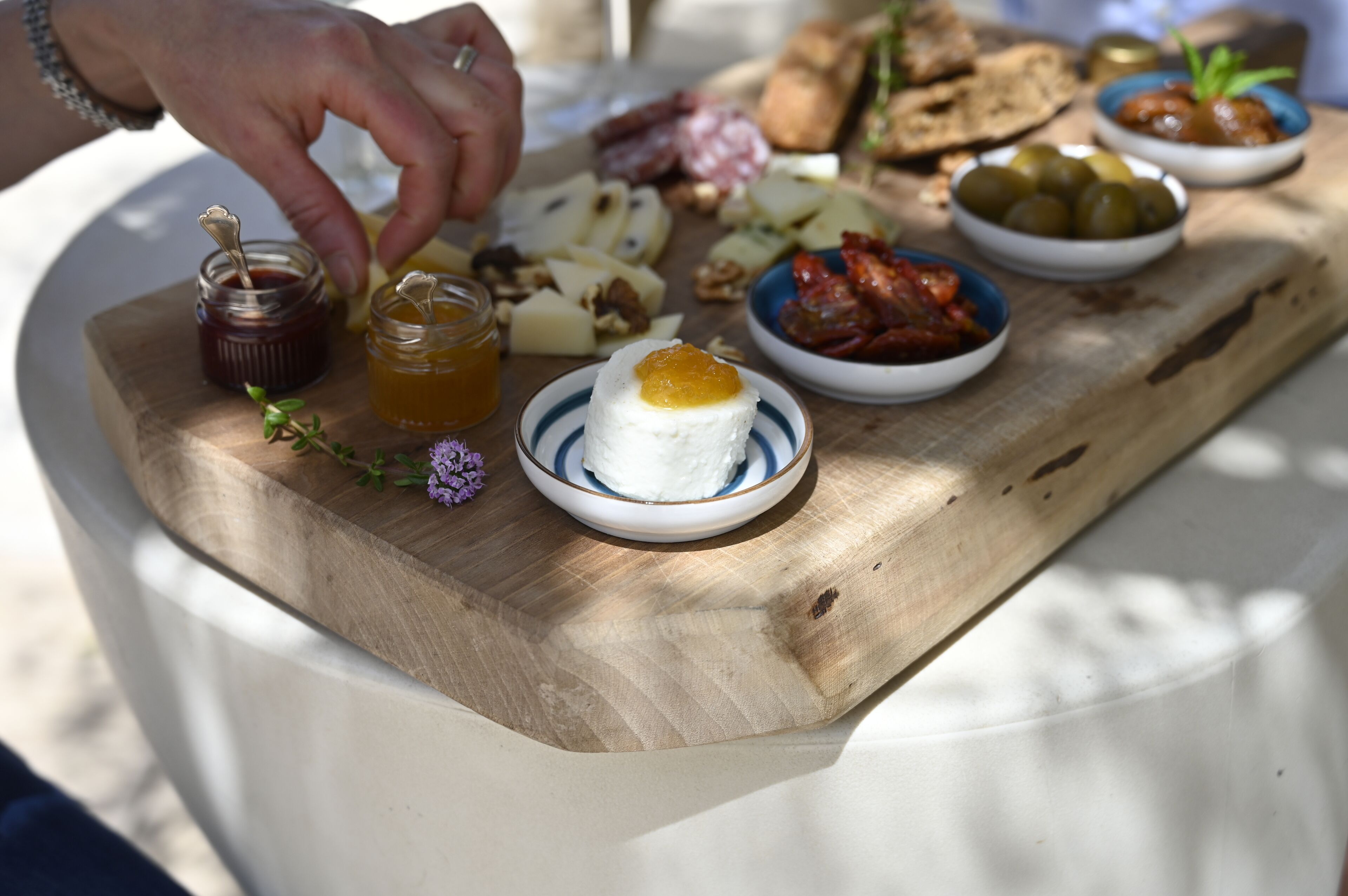 Une planche en bois garnie de différents fromages, d’olives et d’un pot de miel.