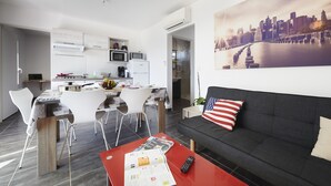 A modern apartment with a dining area, kitchen, and a living room with a sofa and a cityscape painting. - Les Gîtes de la Galaure (Châteauneuf-de-Galaure)