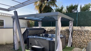 A hot tub with a canopy, surrounded by a stone wall and a grassy area. - Les Gîtes de la Galaure (Châteauneuf-de-Galaure)