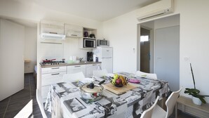 A compact kitchen with white cabinets, a microwave, a toaster, and a coffee maker. A dining table with a newspaper-themed tablecloth is set with chairs. - Les Gîtes de la Galaure (Châteauneuf-de-Galaure)
