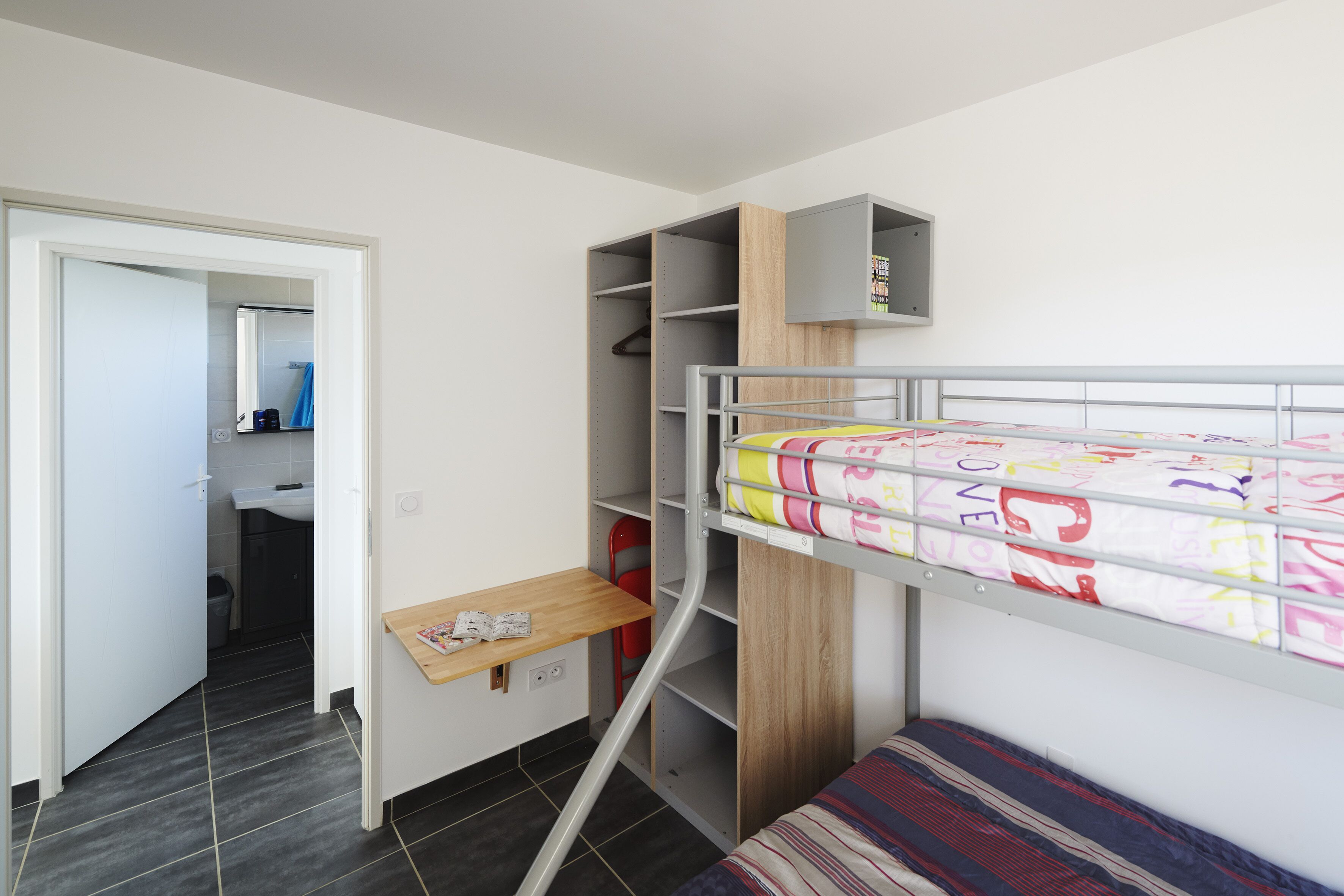 Ein kleines Schlafzimmer mit Etagenbett, Schreibtisch und eingebautem Kleiderschrank.