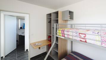 Ein kleines Schlafzimmer mit Etagenbett, Schreibtisch und eingebautem Kleiderschrank.