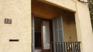 A building entrance with a number '12' sign, a door with shutters, and a small balcony with a metal railing. - Studio for rent in LUMIO in BALAGNE (Lumio)