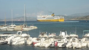 A marina with various boats docked, a ferry in the background, and a mountainous coastline. - Studio for rent in LUMIO in BALAGNE (Lumio)