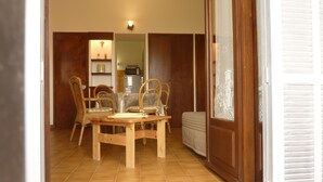 A dining area with a wooden table and chairs, a kitchen in the background, and a sliding glass door leading to a balcony. - Studio for rent in LUMIO in BALAGNE (Lumio)