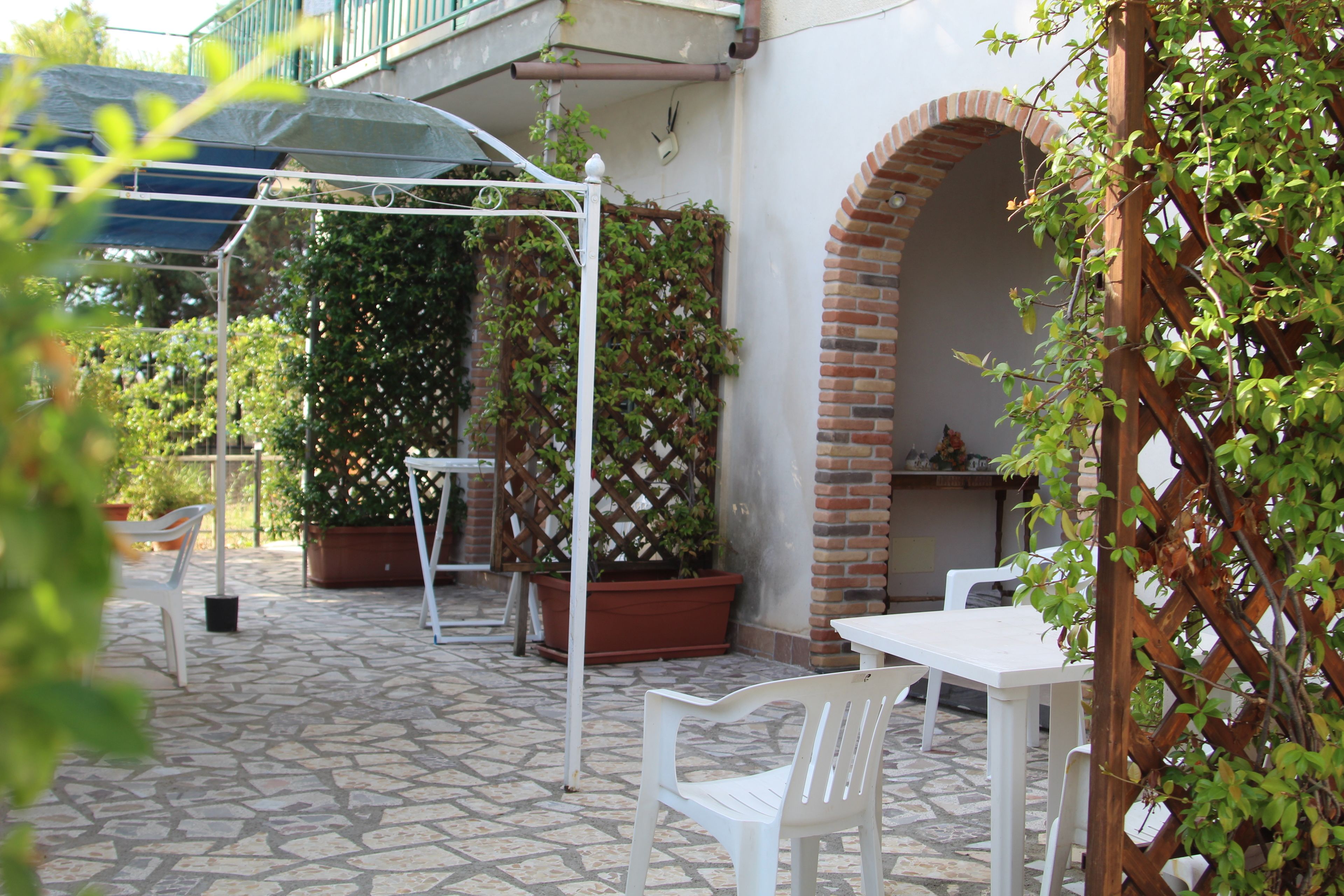 An outdoor patio with a white table and chairs, a brick archway, and potted plants.