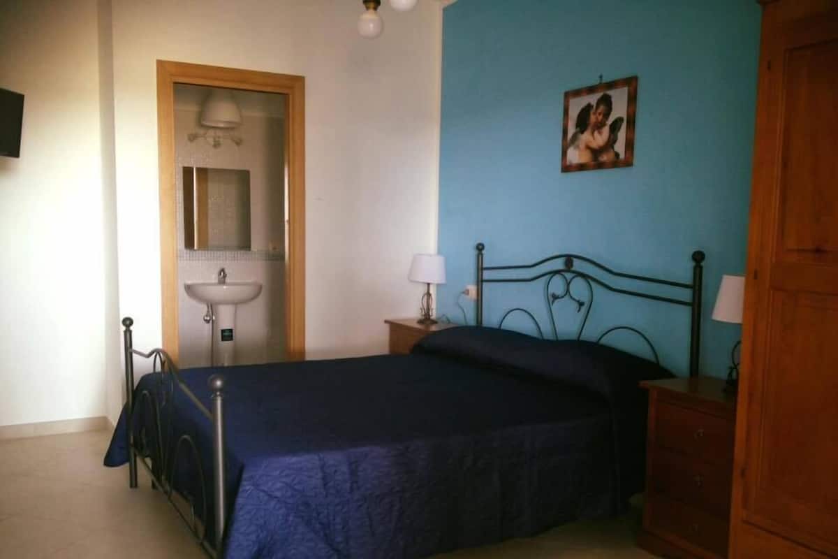 A bedroom with a bed, a nightstand, a dresser, a sink, and a mirror.