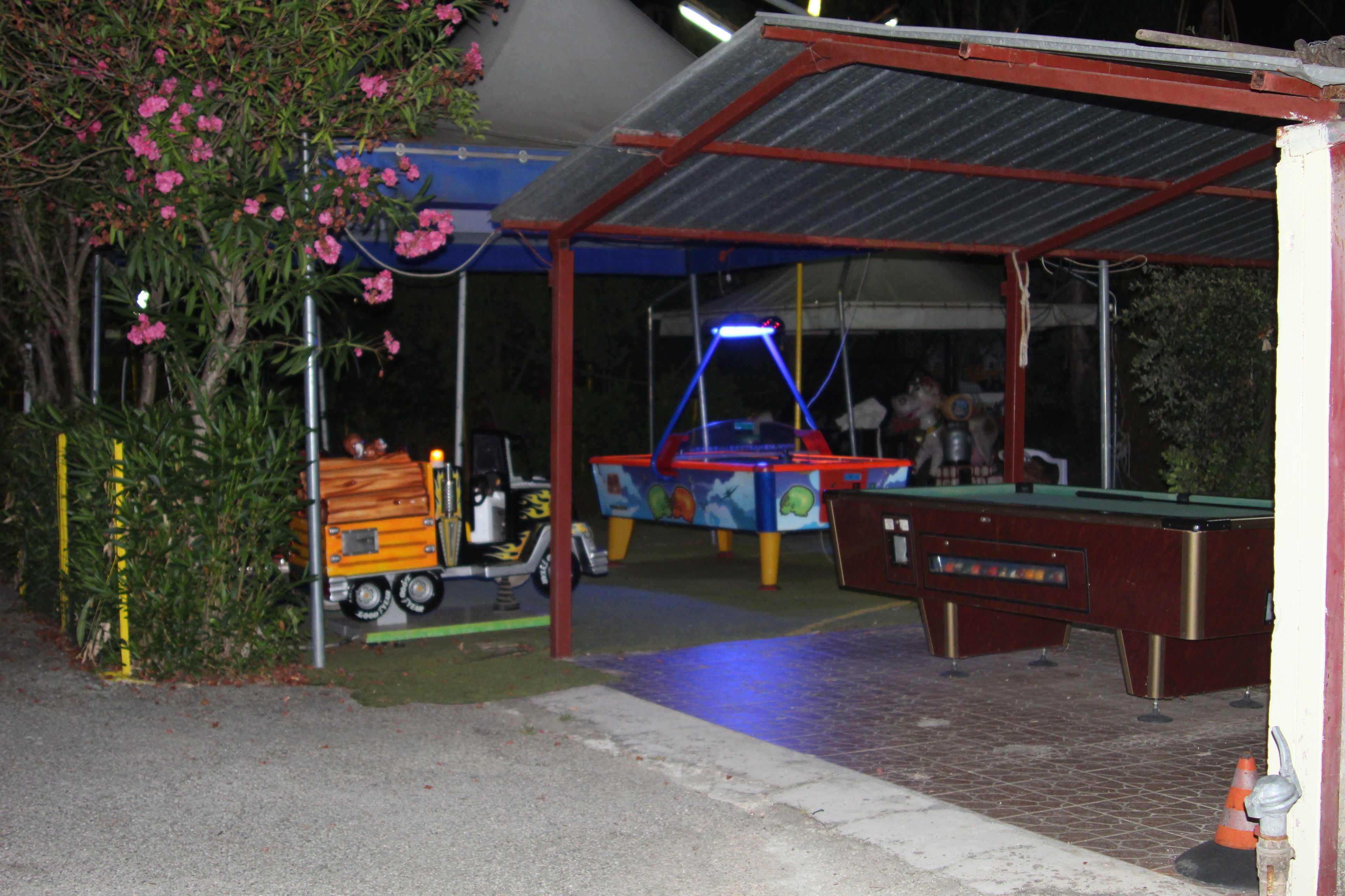 A covered outdoor area with a pool table, a small vehicle, and a building with a red roof.