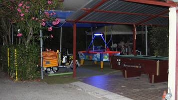 A covered outdoor area with a pool table, a small vehicle, and a building with a red roof.