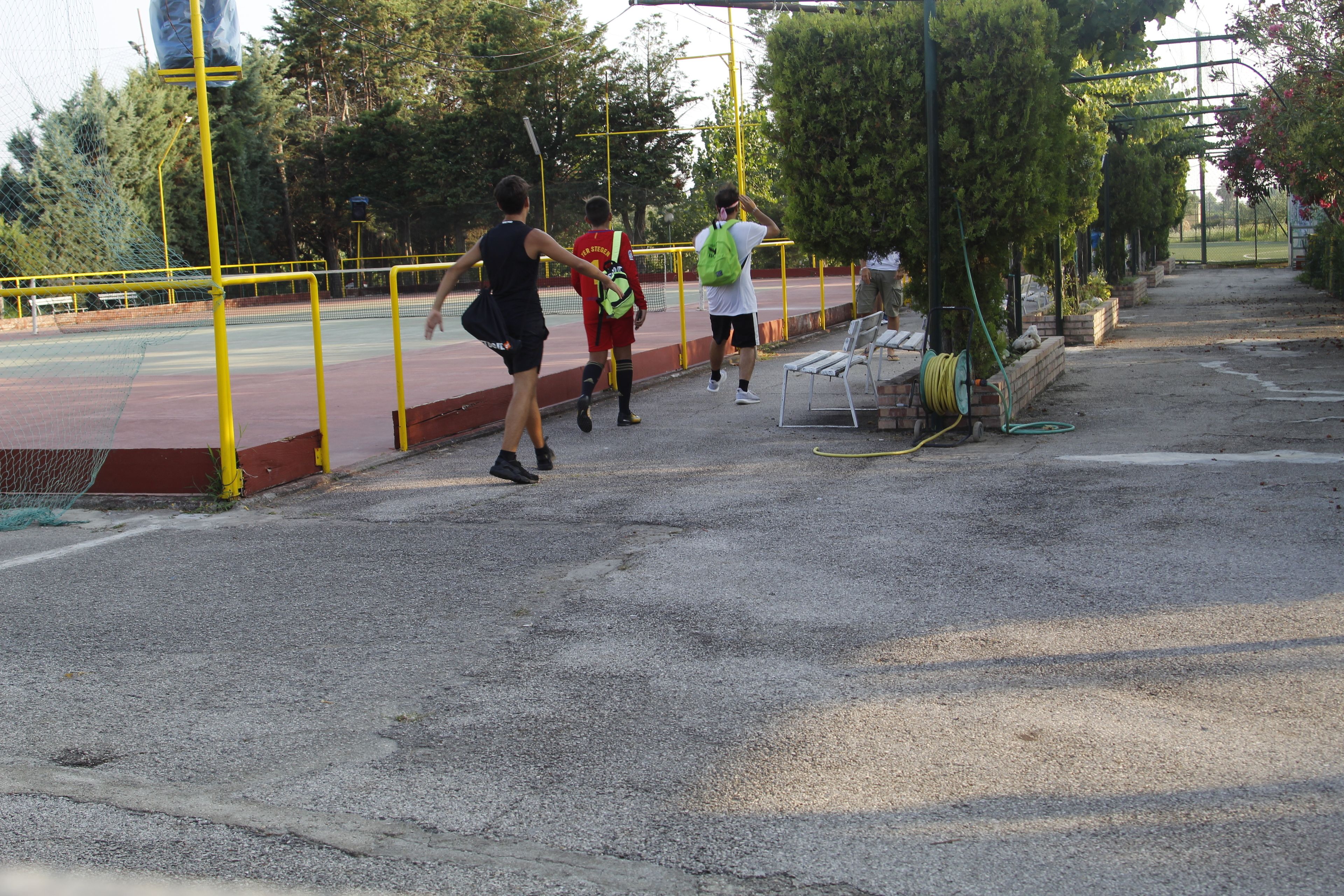 Una cancha de tenis con una red, barandillas amarillas y algunas personas caminando.