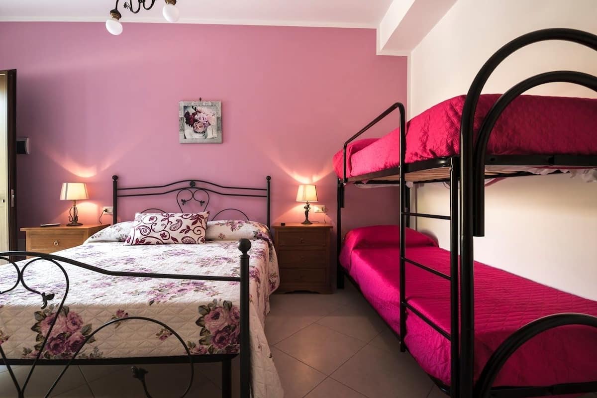 A bedroom with a bunk bed, a single bed, two bedside tables with lamps, and a wall-mounted picture.
