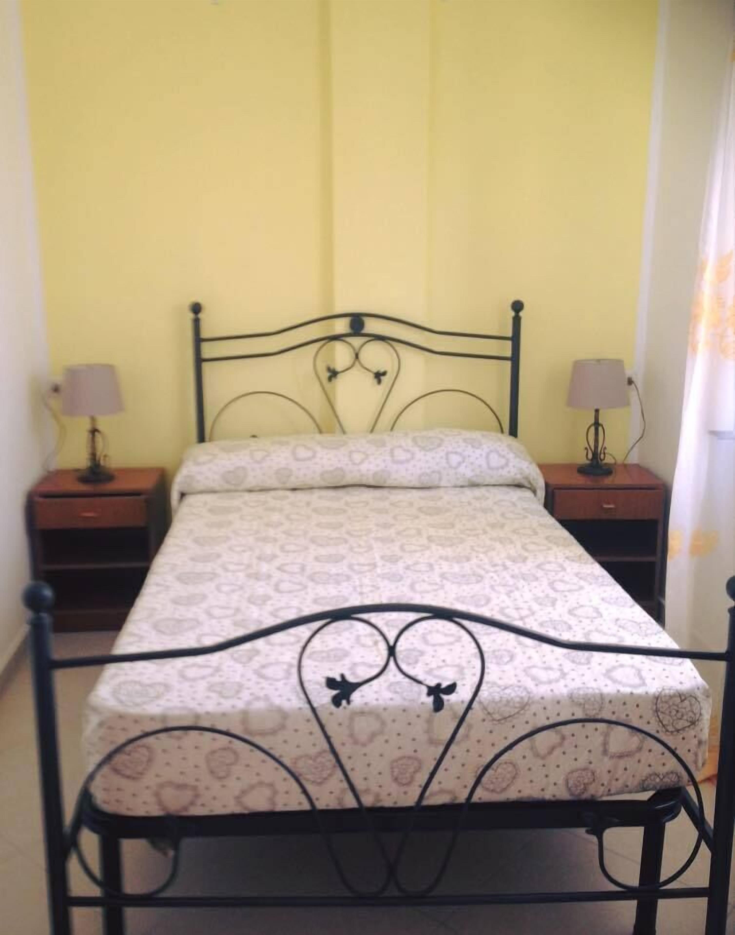 A single bed with a metal frame and heart-patterned bedding in a room with yellow walls.
