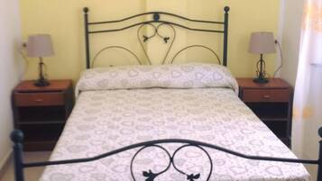 A single bed with a metal frame and heart-patterned bedding in a room with yellow walls.