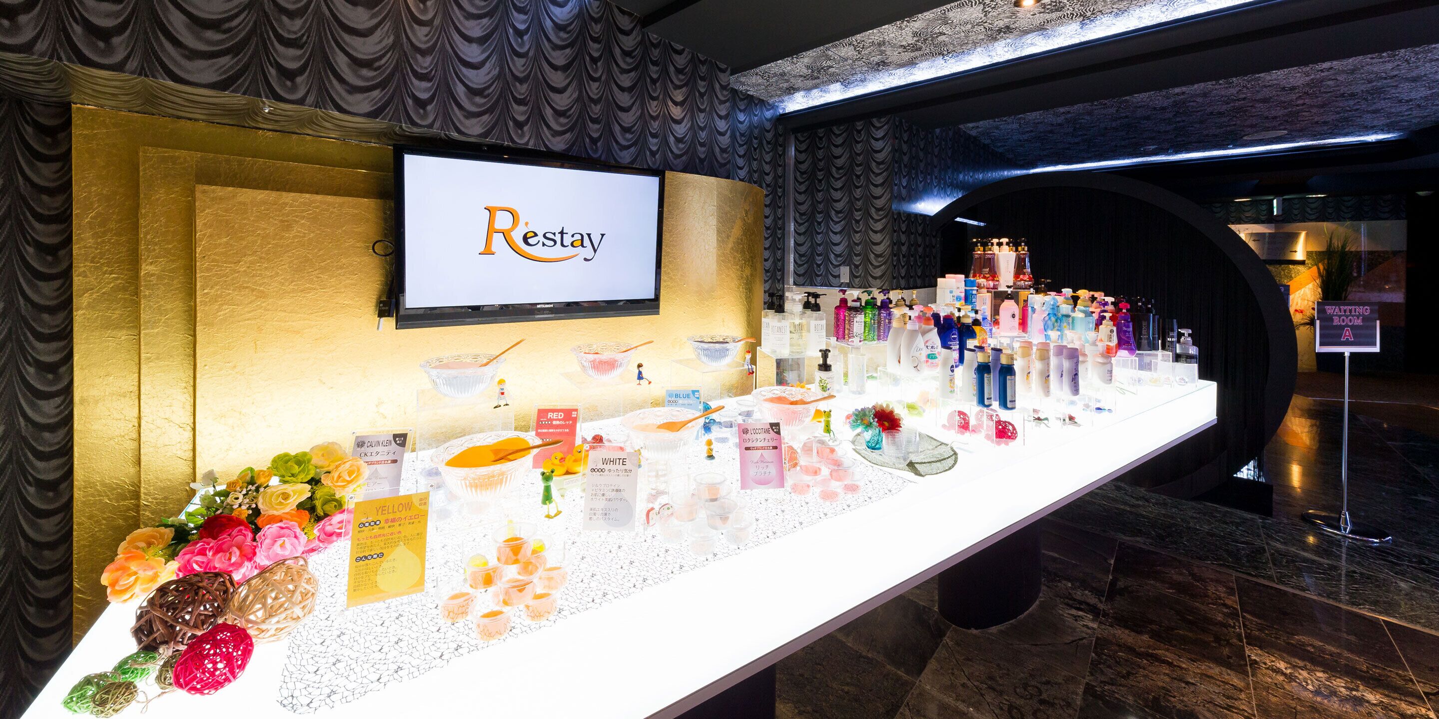Zona de recepción con un cartel de 'Restay', exhibición de artículos de aseo y señalización de sala de espera.