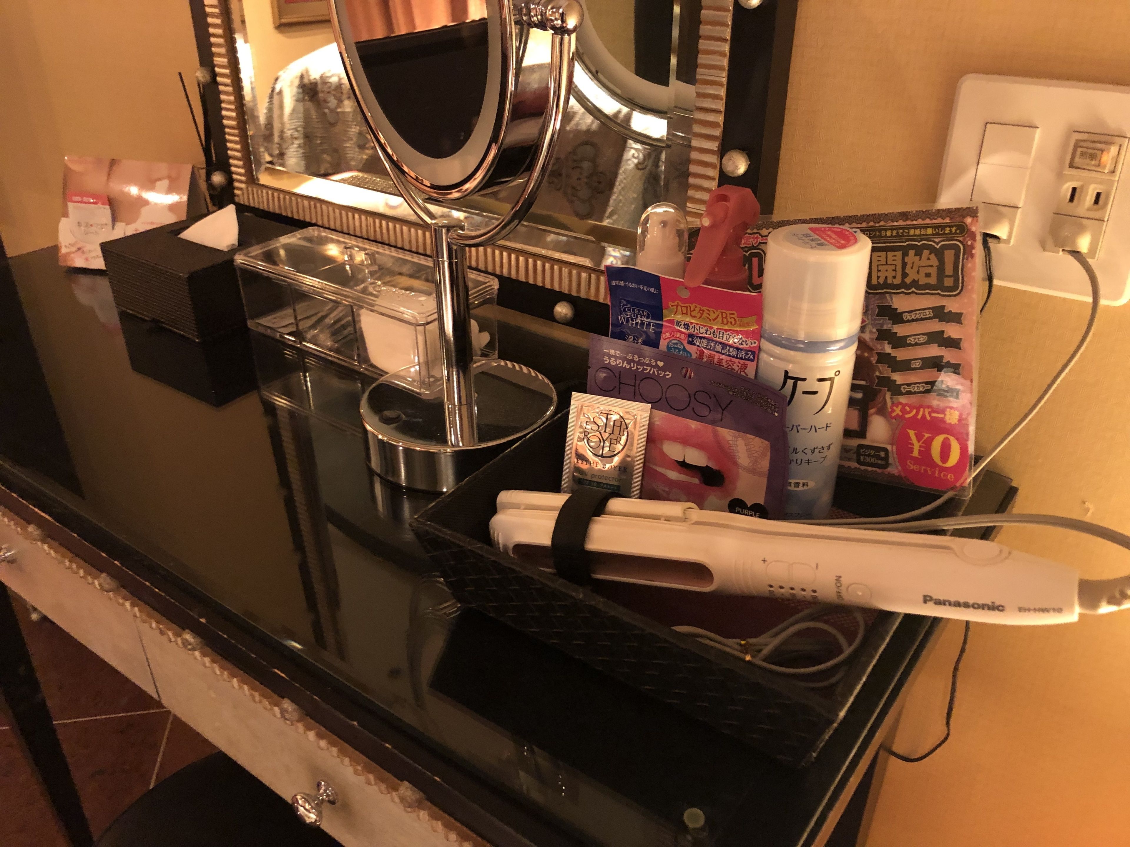 Ein Badezimmer-Waschtisch mit einem Föhn, einer Shampooflasche, einer Zahnpastatube und einem Spiegel.