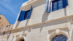 A building with a beige facade, blue shutters, and a decorative arched window. - The Suites - Piazza Kirkop (Kirkop)