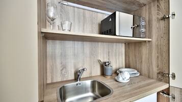 A kitchen with a stainless steel sink, wooden shelves, and a microwave.