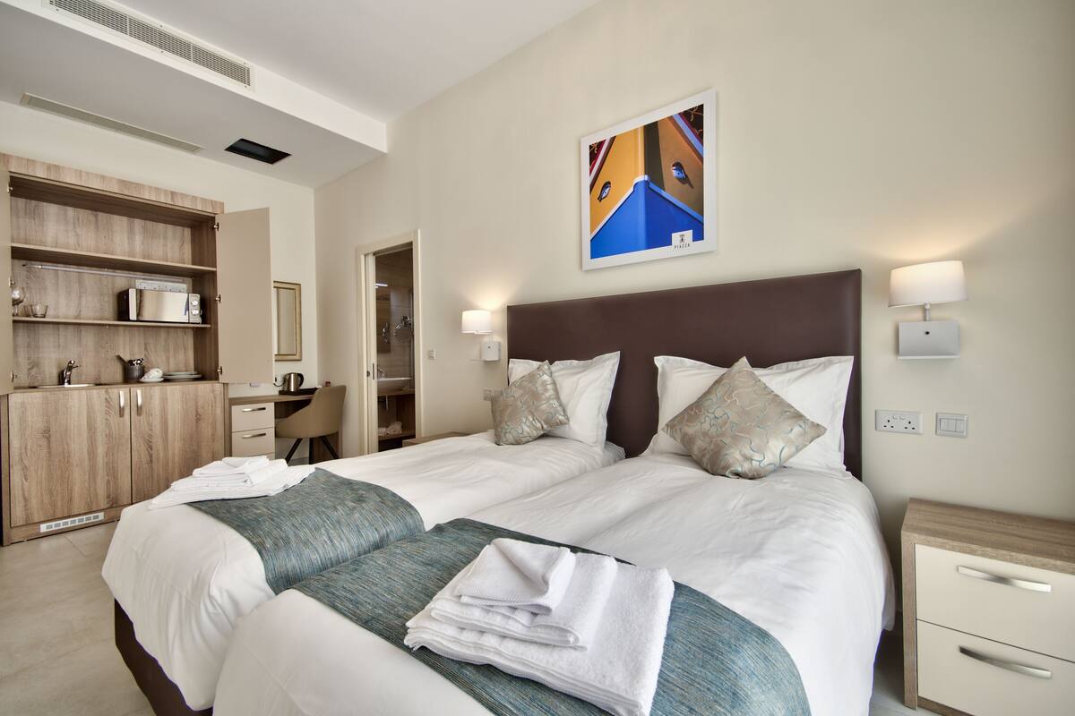 A hotel room with a large bed, a desk, a wardrobe, and a painting on the wall.