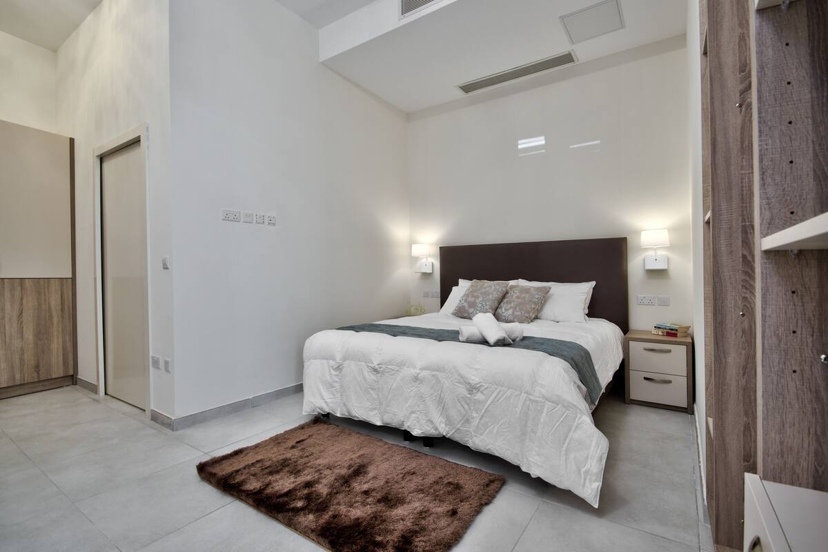 A modern bedroom with a large bed, bedside lamps, a nightstand, and a fluffy rug.