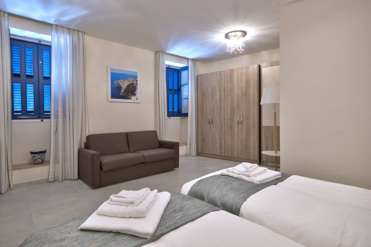 A hotel room with a bed, a sofa, a wardrobe, and a window with curtains.