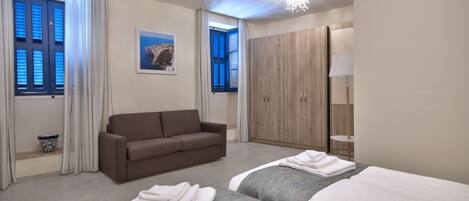 A hotel room with a bed, a sofa, a wardrobe, and a window with curtains.