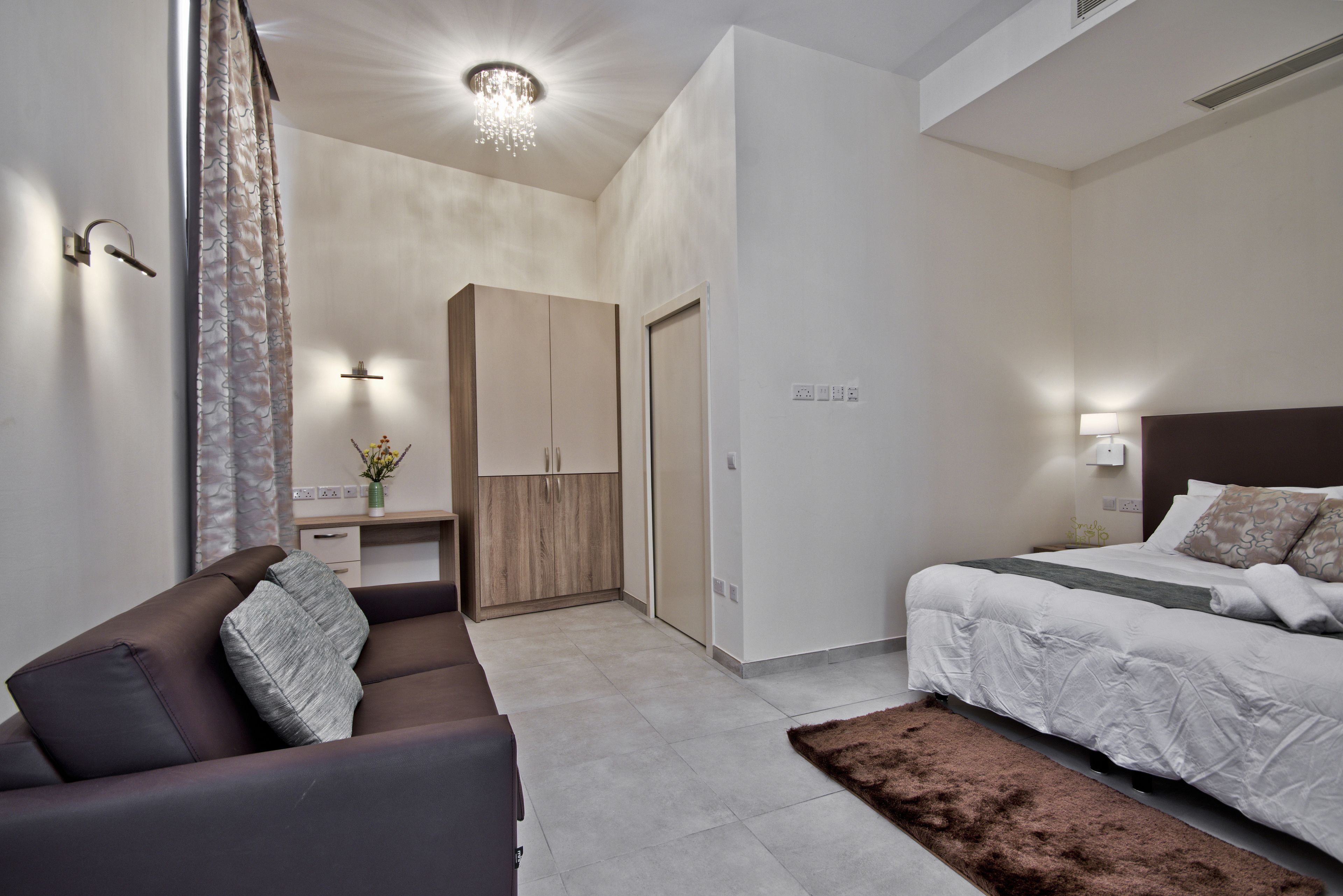 Een moderne slaapkamer met een bed, een bank, een bureau en een kledingkast.