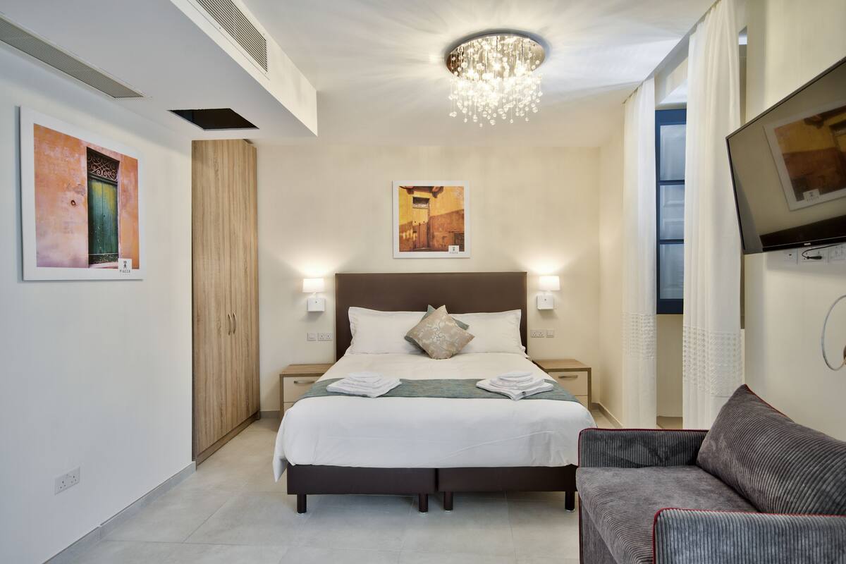 A hotel room with a large bed, two bedside tables, a TV, and artwork on the walls.