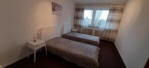 A small, clean room with two single beds, a bedside table, a radiator, and a window with curtains. - Appartement 62 qm, Central (Hannover)