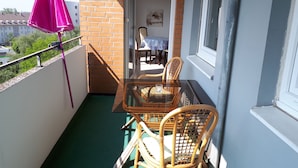 Un balcon avec une table en verre et des chaises en osier, un parasol violet et une vue sur un bâtiment en arrière-plan.