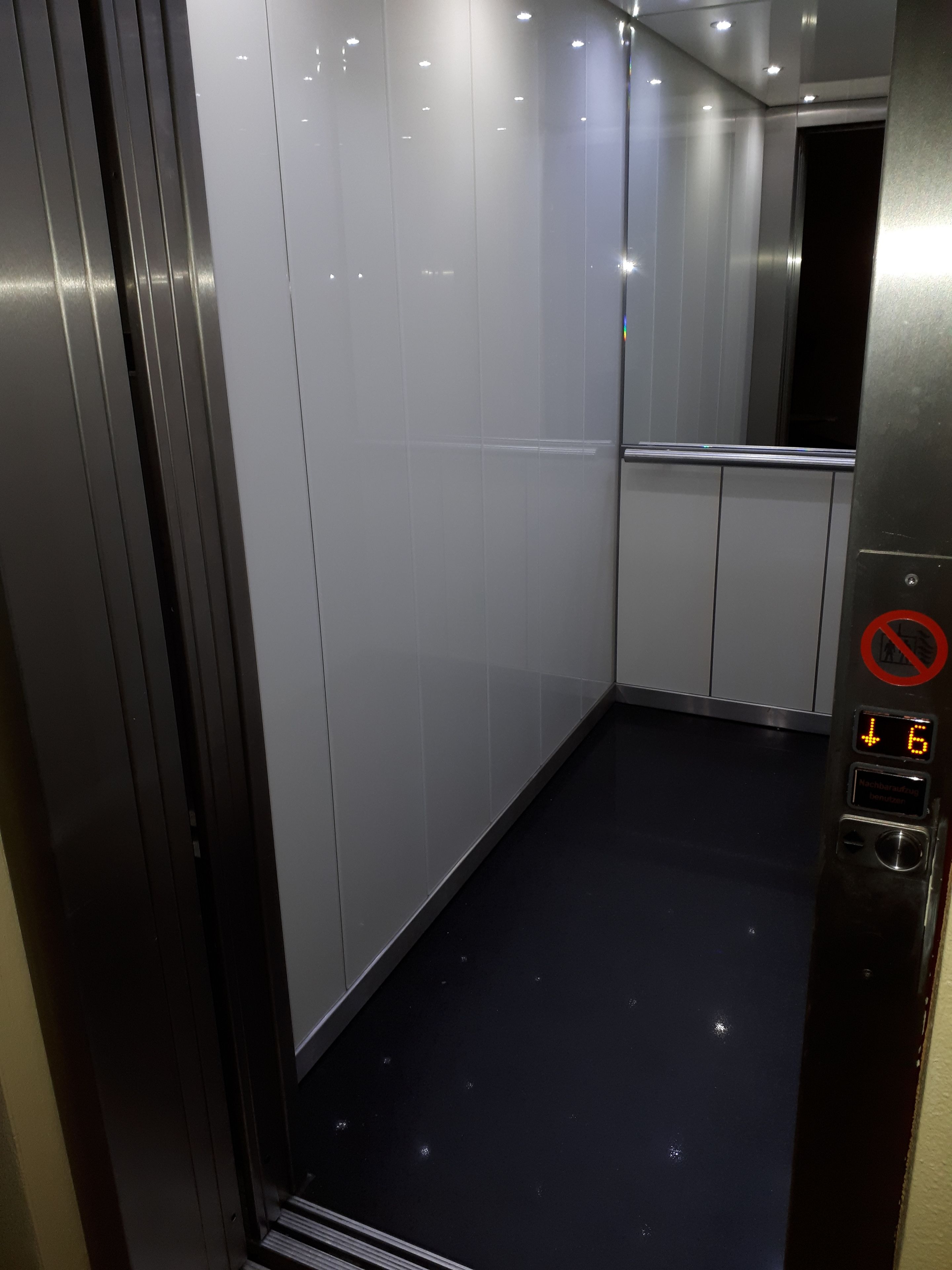 An elevator interior with a digital display showing the floor number, a no-smoking sign, and a button panel.