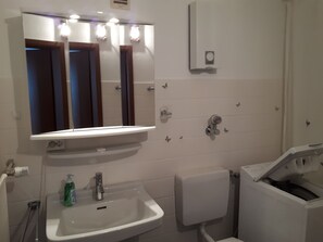 A bathroom with a white sink, a mirror, a toilet, and a washing machine. - Appartement 62 qm, Central (Hannover)