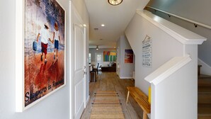 A hallway with a wooden bench, a colorful abstract painting, and a poster with beach-related text. - Shared Heated Pool with Water Slide, Golf Cart Access (Port Aransas)