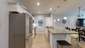 A modern kitchen with a stainless steel refrigerator, granite countertops, and a central island with bar stools. - Shared Heated Pool with Water Slide, Golf Cart Access (Port Aransas)